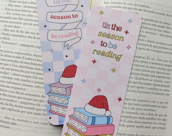 Op de afbeelding: Twee feestelijke bladwijzers met de tekst "tis the season to be reading". Eén bladwijzer heeft een kerstmuts bovenop een stapel boeken en een cadeau. De andere heeft de tekst op een banner.