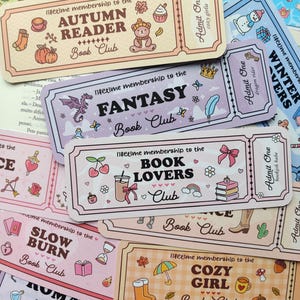Op de afbeelding: Een verzameling kleurrijke bladwijzers in ticketstijl met verschillende thema's zoals Kerstmis, Autumn Reader, Fantasy, Book Lovers en Cozy Girl. Elke bladwijzer heeft unieke illustraties en de tekst "lifetime membership to the Book Club."