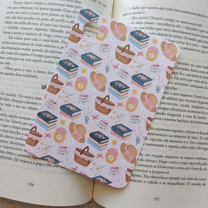 Può includere: Un segnalibro decorativo con un motivo ripetuto di cestini da picnic, libri, tazze da tè, cappelli e fiori in colori pastello. Il segnalibro è posto su un libro aperto.