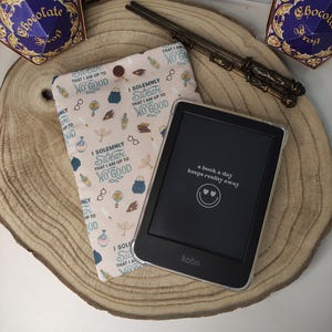 Può includere: Una custodia per e-reader rosa e bianca con un design a tema Harry Potter. La custodia presenta un motivo di pozioni, occhiali e il testo "Giuro solennemente che non sono all'altezza di niente di buono". L'e-reader è di marca Kobo e ha uno schermo nero con il testo "un libro al giorno tiene lontana la realtà" visualizzato.