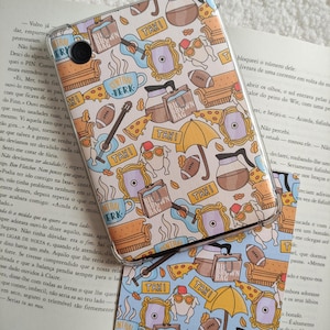 Può includere: Una custodia per telefono blu e gialla con un motivo ripetuto di immagini dello show televisivo popolare "Friends". Le immagini includono il famoso divano arancione, una caffettiera, una fetta di pizza, una chitarra, un taxi, una tazza di caffè con le parole "Central Perk" e un sacchetto di carta marrone con le parole "Blue Brown Bag".