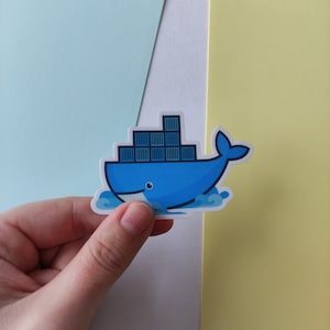 Peut inclure: Un autocollant de baleine bleue avec une pile de conteneurs sur son dos. La baleine nage dans une vague. L'autocollant est sur un fond bleu clair, blanc et jaune.