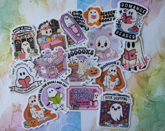 May include: A collection of colorful stickers featuring cartoon ghosts reading books. The stickers have various designs, including ghosts in a bookstore, reading in bed, and with pumpkins. Text includes "Romance Reader" and "Book Shopping is my Therapy."