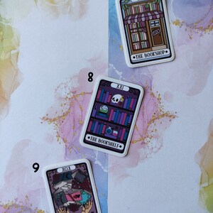 K&ouml;nnte beinhalten: Drei Tarotkarten-Aufkleber mit violetten, rosa und blauen Designs. Die Karten sind mit 7, 8 und 9 nummeriert. Die Kartentitel lauten "The Bookshop", "The Bookshelf" und "The Collector".