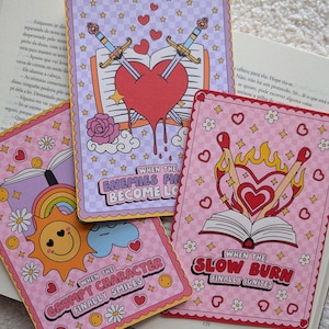 Puede incluir: Cuatro tarjetas ilustradas coloridas con temas románticos. Una tarjeta presenta espadas cruzadas a través de un corazón, otra muestra un sol con una cara sonriente y una tercera representa un corazón con llamas. El texto incluye "When the Enemies Become Lovers" y "When the Grumpy Character Finally Smiles."