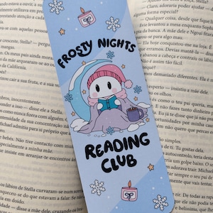 Op de afbeelding: Lichtblauw bladwijzer met de tekst "FROSTY NIGHTS READING CLUB". Het toont een stripfiguur die leest onder een maan, sneeuwvlokken, sterren en een kaars.