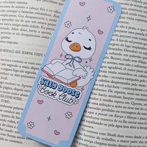 Könnte beinhalten: Ein Lesezeichen mit einer Cartoon-Gans, die ein Buch liest, mit dem Text "Silly Goose Book Club". Das Lesezeichen hat einen hellrosa Hintergrund mit blauen Rändern, Herzen, Sternen und Blumenakzenten.