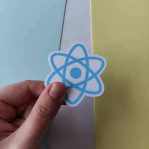 Peut inclure: Un autocollant bleu et blanc avec un symbole d'atome. L'autocollant est tenu par une main sur un fond bleu clair, blanc et jaune.