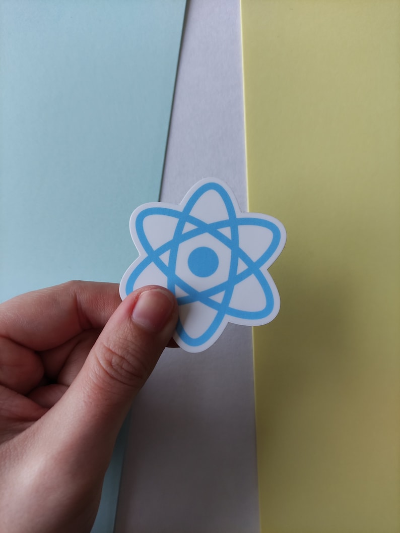 Peut inclure: Un autocollant bleu et blanc avec un symbole d'atome. L'autocollant est tenu par une main sur un fond bleu clair, blanc et jaune.