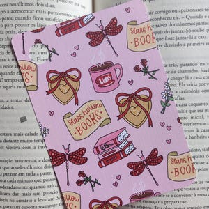 Pode incluir: Marcador de livros rosa com um padrão repetido de corações, libélulas, livros, rosas e canecas de café. O texto "Stars Hollow Books" é visível. Um item decorativo para amantes de livros.