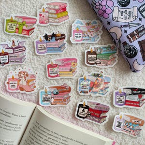 May include: A collection of colorful stickers featuring stacks of books with candles on top. The stickers have different titles and genres, including "Sweethearts", "Fantasy", "Cowboy Romance", "Historical Romance", "Morally Gray", "Plot Twist", and "Chosen One".