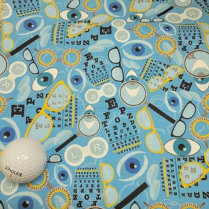 May include: A blue fabric with a repeating pattern of eyeglasses, eye charts, and eyeballs. The eye charts feature the letters E, F, O, P, Z, and D. The fabric is perfect for crafting projects like quilting, sewing, and scrapbooking.