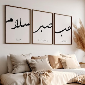 Może przedstawiać: Trzy oprawione wydruki z kaligrafią arabską i napisami "PAIX", "PATIENCE" i "AMOUR" umieszczonymi pod każdym wydrukiem. Wydruki wiszą na białej ścianie nad łóżkiem z brązowymi poduszkami.