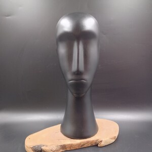 May include: A black ceramic mannequin head with a smooth, matte finish. The head is mounted on a wooden base.
