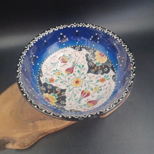 May include: A blue and white ceramic bowl with a floral design. The bowl has a black rim and a white interior with a floral pattern in shades of red, yellow, and green.
