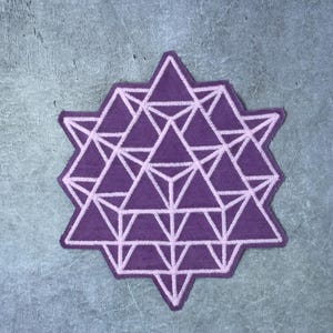 May include: A fabric patch featuring a deep purple base with a light pink embroidered geometric pattern. The design consists of a complex arrangement of interconnected triangles forming a star-like shape with sharp points and symmetrical lines.