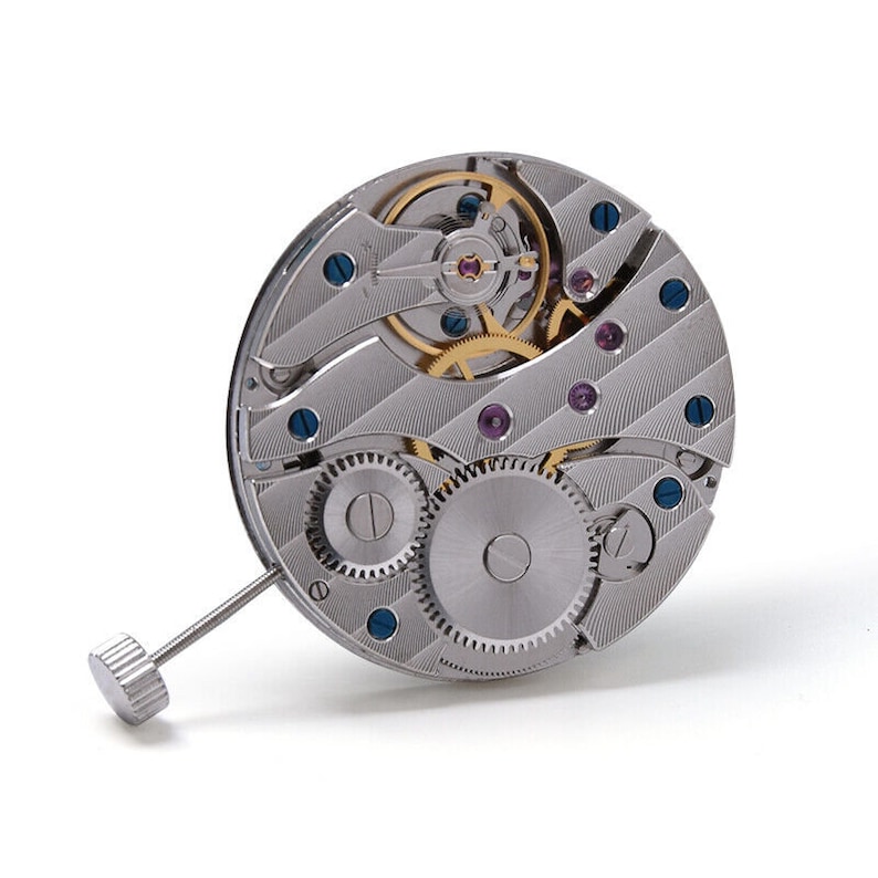 K&ouml;nnte beinhalten: Ein silbernes Uhrwerk mit komplizierten Zahnr&auml;dern und einer Aufzugsfeder. Das Uhrwerk ist freigelegt und zeigt die inneren Funktionsteile der Uhr.