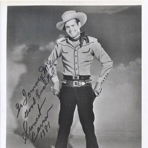 May include: Black and white photograph of a man wearing a cowboy hat and a button-down shirt. He is standing with his hands in his pockets. The photo is signed "To Johnny,  Good Luck &  Sincerly,  Cannon  1961".