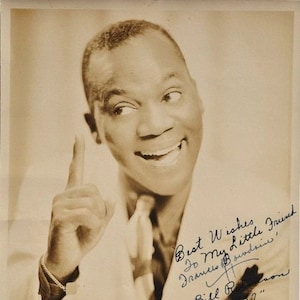 May include: Black and white photo of a man smiling and pointing with his right index finger. He is wearing a white shirt and a dark tie. The photo is signed "Best Wishes to My Little Friend, Frances Sundries, Bill Robinson 1937."