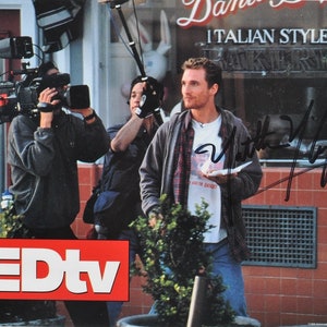 May include: A black and white photo of a man holding a paper bag with a white rabbit on it. He is wearing a plaid shirt and jeans. The photo is signed "Matt Damon".