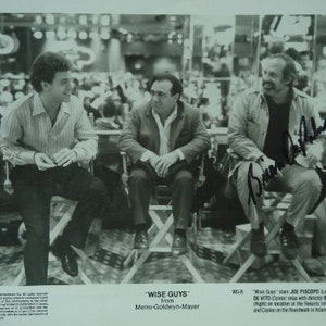 Może przedstawiać: Czarno-białe zdjęcie trzech mężczyzn siedzących na krzesłach. Mężczyźni wszyscy się uśmiechają i patrzą w obiektyw. Zdjęcie jest podpisane przez Briana De Palmę. Tekst "Wise Guys" z Metro-Goldwyn-Mayer jest wydrukowany pod zdjęciem.