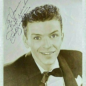 May include: A black and white photo of a young man wearing a tuxedo with a bow tie. He is smiling and looking at the camera. The photo is signed "To Joanne, Best Wishes, Frank Sinatra".