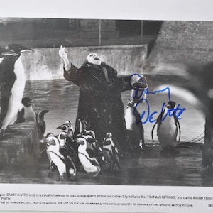 Może przedstawiać: Czarno-białe zdjęcie przedstawiające Danny'ego DeVito jako Pingwina z filmu "Powrót Batmana". Jest otoczony przez pingwiny, z jego autografem w niebieskim tuszu. Zdjęcie jest kadr z filmu promocyjnego.