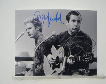 May include: Black and white photo of two musicians, one playing an acoustic guitar. The photo is signed by both musicians, "Paul McCartney" and "John Lennon".