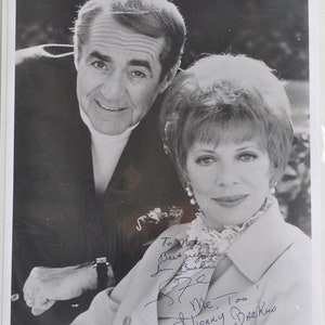 Puede incluir: Foto en blanco y negro de un hombre y una mujer, ambos sonriendo. La mujer lleva una blusa blanca y una chaqueta clara. El hombre lleva un suéter oscuro. La foto está firmada "To Mike, Best regards, Jon Buckner, & Me Too,  Penny Buckner".