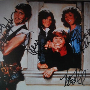 May include: A signed photograph of four people, possibly actors, framed by a window. The image is signed with a black marker. The photograph has a warm, nostalgic tone, suggesting it is a vintage item.