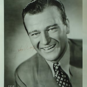 Peut inclure: Photo publicitaire en noir et blanc de John Wayne, souriant, portant un costume et une cravate. La photo est signée "John Wayne" à l'encre rouge. Le texte "John Wayne in, "SEVEN SINNERS", a Universal Production, Printed in U.S.A." est en bas de la photo.