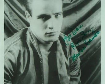 May include: Black and white photo of a man with short dark hair wearing a jacket. The man is looking at the camera with a serious expression. The photo is signed "For Dan,  R. Brando"