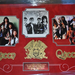 May include: A framed red background with three black and white photos of the band Queen. The photos are surrounded by gold trim. The band's crest is in the center of the frame. The text "Queen" is in gold lettering at the bottom of the frame. The text "Original Ink Signatures by Queen Band Members Freddie Mercury Brian May John Deacon Roger Taylor" is at the bottom of the frame.