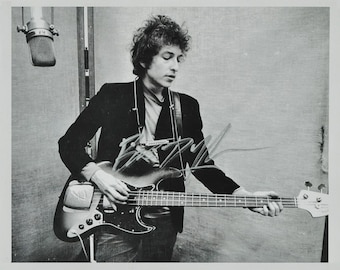 May include: Black and white photo of a musician playing a bass guitar. The musician is wearing a black jacket and a white shirt. The photo is signed by the musician.