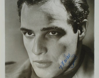 May include: Black and white publicity photo of Marlon Brando. The image is a close-up of his face, with a signature in blue ink. The film title "THE MEN" is visible at the bottom.