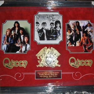 May include: A framed Queen band memorabilia featuring a red background with gold accents. The frame includes three photos of the band members, a gold Queen crest, and the band's name in gold lettering. The photos include a group shot of the band, a close-up of the band members' signatures, and a photo of the band performing on stage. The text below the photos reads "Original UK Exclusive Band Members Freddie Mercury, Brian May, John Deacon, Roger Taylor."