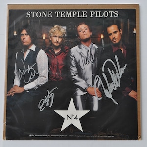 May include: A black and white photograph of the band Stone Temple Pilots, signed by all four members. The band members are standing in front of a black background with candles. The album cover for their album "No. 4" is visible in the bottom centre of the photo.