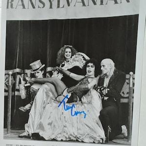 May include: A black and white photograph of a scene from the film "The Rocky Horror Picture Show". The photo features four actors in costume, including Tim Curry as Dr. Frank-N-Furter. The photo is signed by Tim Curry.