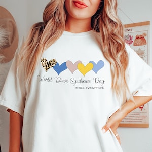May include: White t-shirt with a graphic of five colorful hearts and the text "World Down Syndrome Day Three Twenty One".