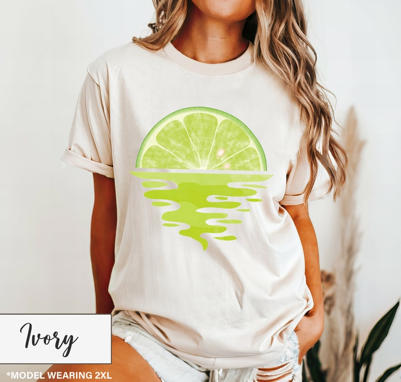 May include: A woman is wearing a light beige t-shirt with a lime wedge graphic. The lime wedge is reflected in the water below it. The text "Ivory" is at the bottom of the image.