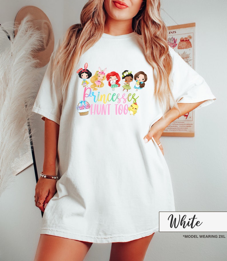 May include: White t-shirt featuring a colorful graphic of cartoon princesses and the text "Princesses Hunt Too." The design includes an Easter basket, chicks, and various princess characters. The shirt is a relaxed fit.