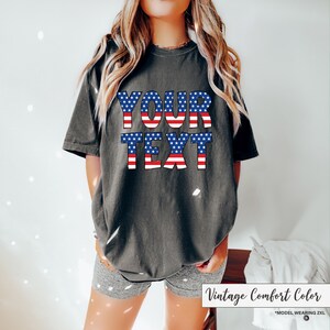 May include: Dark gray t-shirt with the text "YOUR TEXT" in a patriotic red, white, and blue design. The shirt is a vintage comfort color and is a 2XL size.