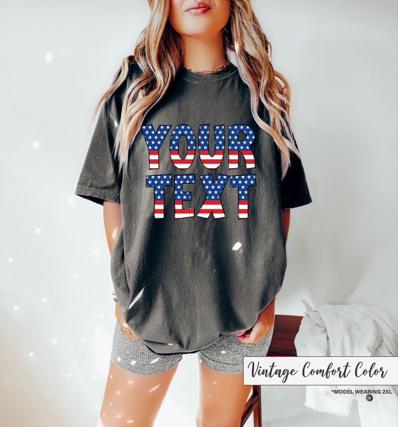 May include: Dark gray t-shirt with the text "YOUR TEXT" in a patriotic red, white, and blue design. The shirt is a vintage comfort color and is a 2XL size.