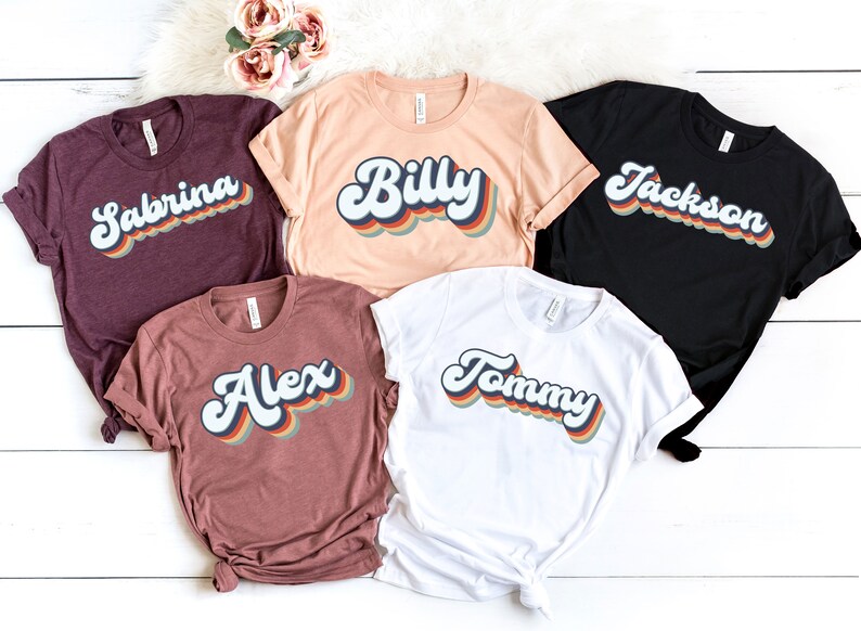 May include: Five t-shirts with different names printed on them in a retro rainbow font. The names are Sabrina, Billy, Jackson, Alex, and Tommy.