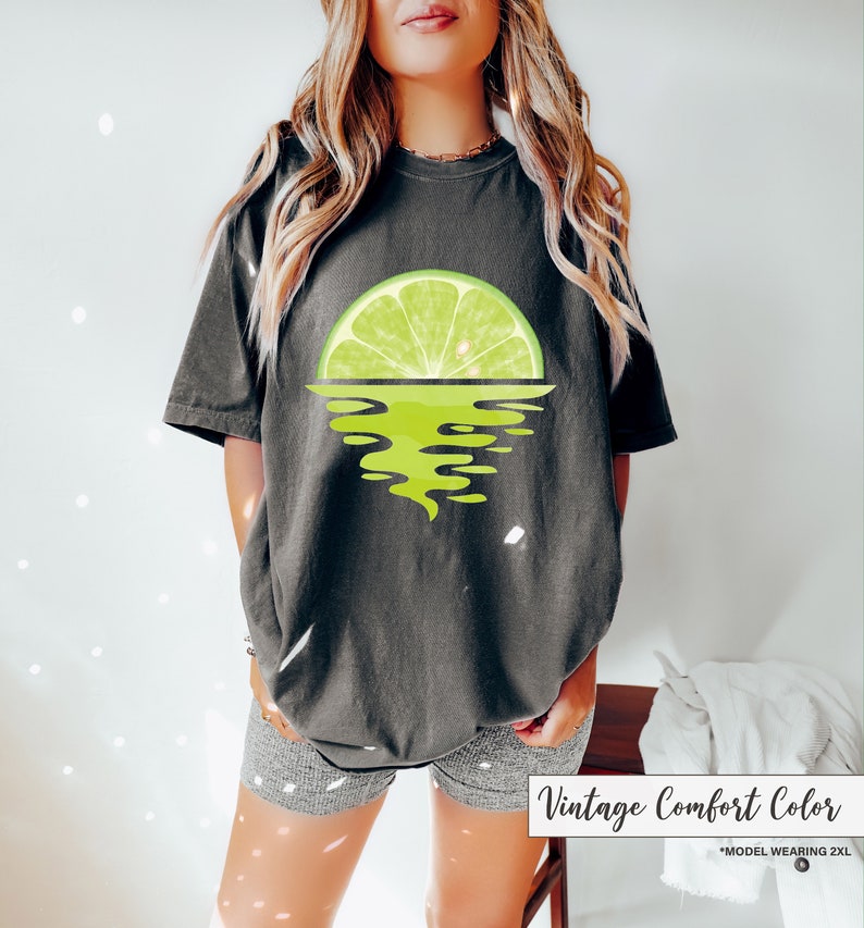 May include: A dark gray t-shirt with a lime wedge graphic. The lime wedge is half submerged in water, creating a sunset effect. The text "Vintage Comfort Color" is printed on the bottom of the image.