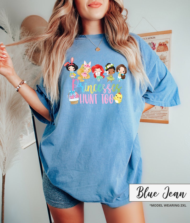 May include: Blue jean colored t-shirt with a graphic of cartoon princesses and the text "Princesses Hunt Too". The shirt is a light blue color and has a relaxed fit. The text "Blue Jean" is in a white box at the bottom.