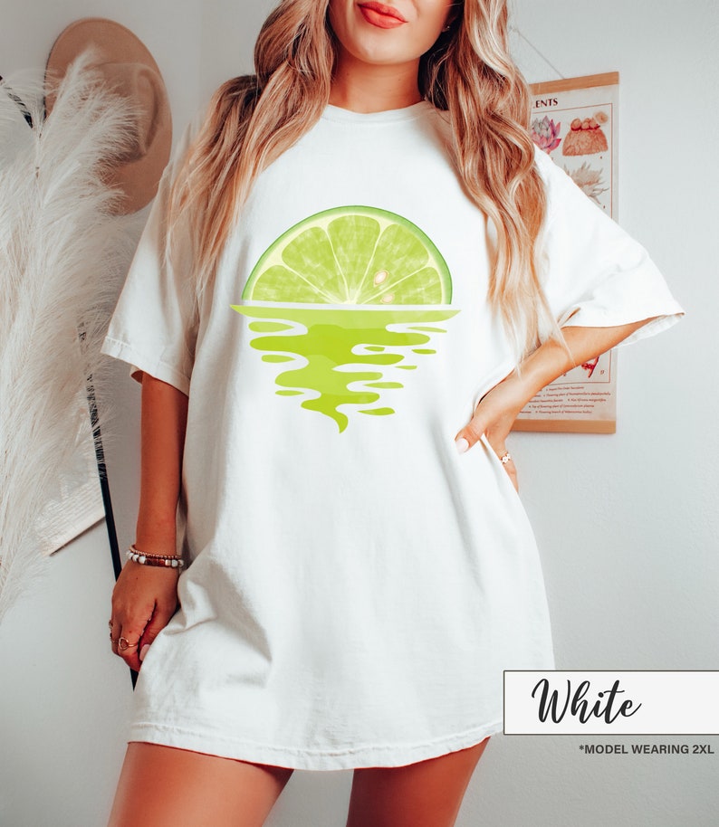 May include: White oversized t-shirt with a graphic of a lime wedge in the water. The text "White" is written in black at the bottom of the image. The text "*MODEL WEARING 2XL" is written in black below the word "White".
