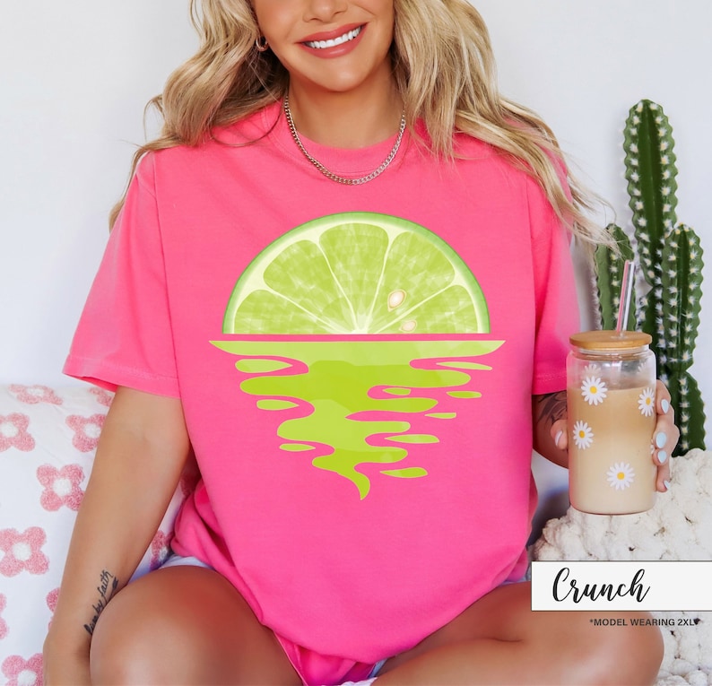 May include: Pink t-shirt with a graphic of a lime wedge over a green and yellow wave design. The text "Crunch" is at the bottom of the image.