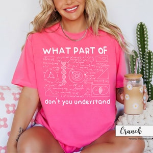May include: A bright pink t-shirt with the text "WHAT PART OF don't you understand" in white. The shirt features a complex scientific diagram design. The model is wearing a 2XL size.