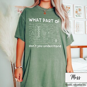 May include: Moss green t-shirt with the text "WHAT PART OF don't you understand" in white. The shirt features a graphic of mathematical and scientific symbols. The model is wearing a 2XL size.
